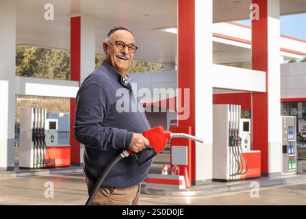 Homme mature souriant tenant un pistolet de ravitaillement dans une station-service libre-service Banque D'Images