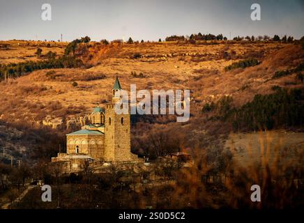 Une église historique en pierre avec un grand clocher situé contre un paysage accidenté de colline. Banque D'Images