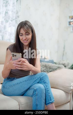 Jeune femme occasionnelle faisant un appel téléphonique tout en étant confortablement assise sur un canapé dans son salon Banque D'Images