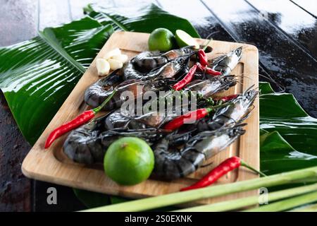 Dans une cuisine tropicale animée, les crevettes tigrées fraîchement pêchées sont magnifiquement exposées sur des feuilles de bananier, accompagnées d'herbes et d'épices parfumées. Banque D'Images