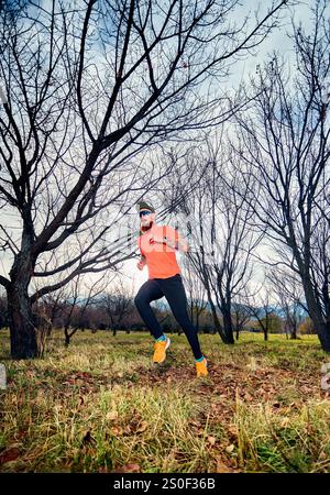 Homme barbu athlétique en chemise rouge courant sur le sentier de sentier dans la forêt d'automne au lever du soleil Banque D'Images