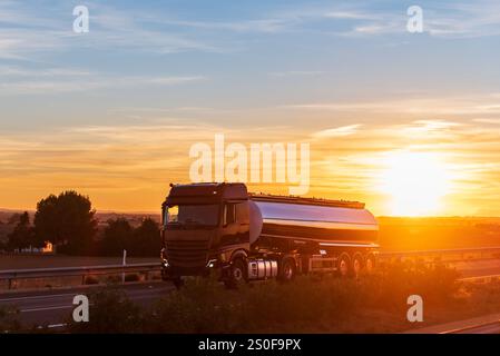 Un camion-citerne de nourriture conduisant sur une autoroute alors que le soleil se couche sur l'horizon, laissant place à la nuit, un travail exigeant sous des vues à couper le souffle. Banque D'Images