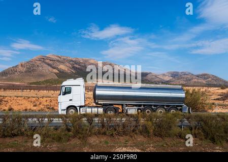 Un camion-citerne de nourriture conduisant sur une route avec un paysage de montagne en arrière-plan, vue de côté. Banque D'Images