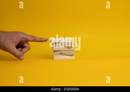 Une image montrant un homme pontant un doigt à un bloc de bois sur trois blocs de plus disposés soigneusement sur un fond jaune Uni. Banque D'Images