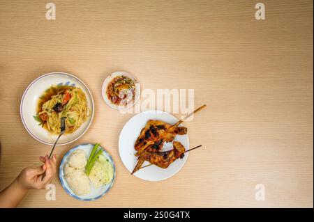 Cuisine thaïlandaise sur table - ensemble de 'somtam' - salade épicée de papaye de style thaïlandais servie avec riz collant, tranches de chou, niébé, poulet grillé dans le bois Banque D'Images