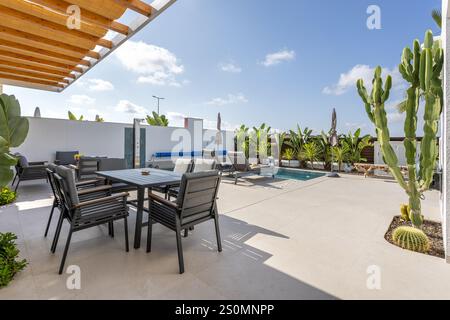 Patio extérieur moderne doté d'un coin repas, de chaises longues, d'une petite piscine, d'un aménagement paysager tropical et d'une pergola à l'ombre. Banque D'Images