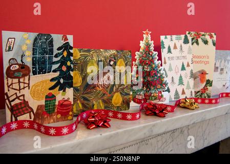 Cartes de Noël affichées sur la cheminée en marbre gris sur fond rouge avec ruban rouge et noeuds recyclés. Banque D'Images