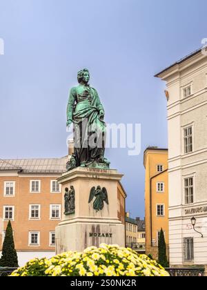 Salzbourg, Autriche - 24 octobre 2024 : statue Mozart en bronze dans sa ville natale de Salzbourg avec de charmants bâtiments et des fleurs. Banque D'Images