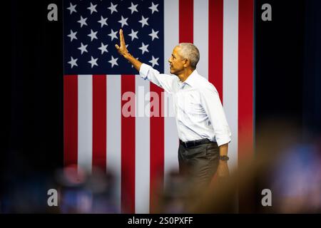 L'ancien président Barack Obama fait des vagues à la foule, debout devant un grand drapeau américain lors d'un rassemblement de campagne démocrate de 2024. Banque D'Images