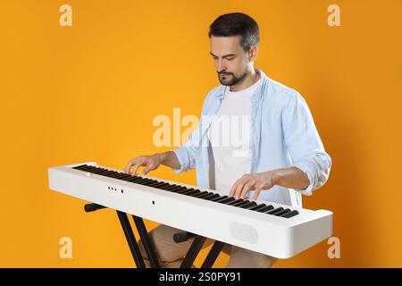 Homme barbu jouant synthétiseur sur fond orange Banque D'Images