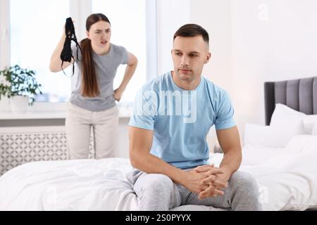 Angry Wife montrant le soutien-gorge de maîtresse comme preuve à son mari infidèle alors qu'il l'ignore dans la chambre, focus sélectif Banque D'Images