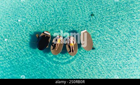Les amis flottent paisiblement sur des transats dans les eaux cristallines de Koh Kood, en Thaïlande. un couple d'hommes et une femme se relaxant sur des transats flottants au-dessus de l'océan Banque D'Images
