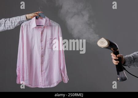 chemise rose vapeur femme avec vapeur à la main sur cintre, gros plan. Banque D'Images