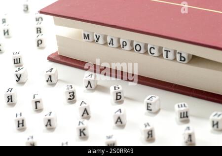 word wisdom written win lettres cyrilliques entre les feuilles de livre et les lettres cyrilliques dispersent sur fond blanc concept abstrait Banque D'Images
