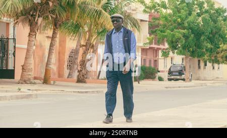 Sant Louis, Sénégal, 2,2018 : photo grandeur nature d'un homme sénégalais typique dans la rue, marchant. Ambiant collonial africain en arrière-plan Banque D'Images
