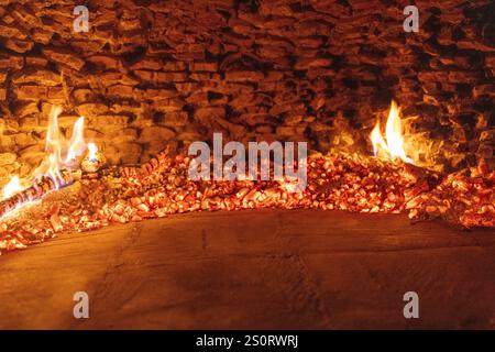 Une vue rapprochée des charbons brillants et des petites flammes à l'intérieur d'un four à bois traditionnel, entouré d'un intérieur rustique en briques Banque D'Images