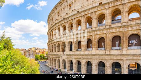 Le majestueux Colisée se trouve bien en vue sous un ciel lumineux à Rome. Les visiteurs admirent son architecture, tandis que les arbres et la vie urbaine animée créent une atmosphère vibrante. Banque D'Images