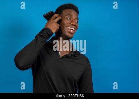 Jeune homme écoutant sur smartphone et souriant sur fond bleu Banque D'Images