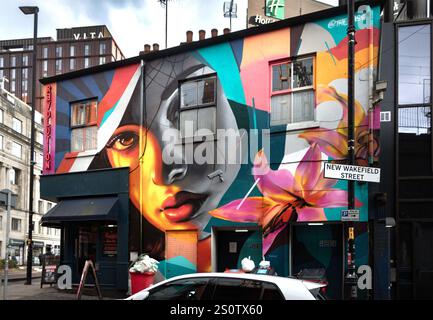 Murale Street art dynamique représentant le visage d'une femme avec des motifs géométriques et floraux colorés sur une façade de bâtiment urbain nouvelle rue wakefield manchester Banque D'Images