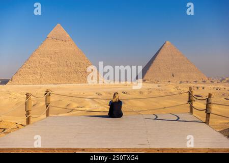 Touriste blonde assis devant les pyramides de Gizeh au Caire, Egypte touriste méditant devant une vue générale des pyramides du plat de Gizeh Banque D'Images