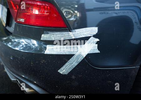 Pare-chocs de voiture fixé avec du ruban adhésif. Extérieur arrière cassé d'une voiture sombre. Réparation provisoire après un accident. Automobile légèrement endommagée en raison d'un accident. Banque D'Images