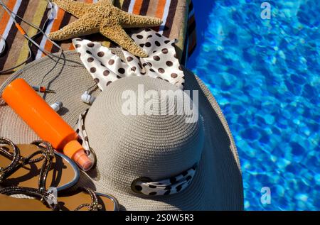 Chapeau pour femmes, sandales, étoiles de mer et écouteurs à côté de la piscine. panama tricoté de raphia sur un fond d'eau bleue Banque D'Images