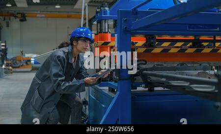 Ingénieure industrielle indienne, avec un casque bleu et des lunettes de sécurité, lors d'une vérification de machines d'usine, gros plan. Concept de maintenance. Banque D'Images