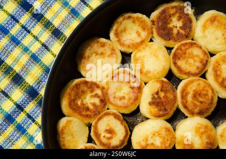 Les cheesecakes faits maison sont frits dans une poêle. Délicieuses crêpes au fromage cottage avec une croûte dorée. Banque D'Images