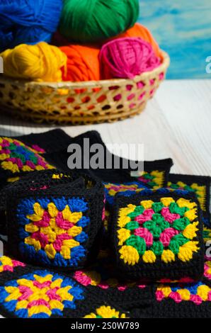 Carré de grand-mère en coton coloré sur fond d'écheveaux multicolores dans un panier en osier. Texture crochet gros plan photo. Tricoté zigzag Banque D'Images