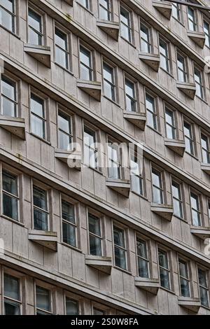Une vue rapprochée en grand angle de l'extérieur d'un bâtiment de plusieurs étages, présentant de nombreuses fenêtres de taille uniforme et de petits balcons à chaque étage, arran Banque D'Images