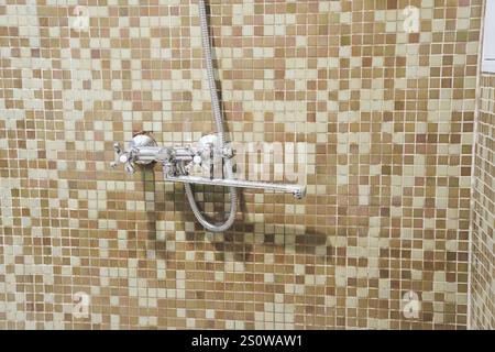 Robinet de douche en gros plan dans la salle de bain sur le fond de carreaux de mosaïque beige. Le concept de style de vie, d'environnement. Photo de haute qualité Banque D'Images