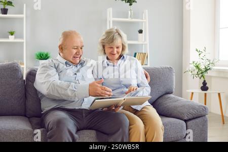 Portrait d'un couple aîné heureux regardant à travers un album photo de famille assis sur le canapé à la maison. Banque D'Images