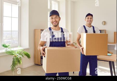 Deux porteurs masculins joyeux du service de déménagement portent des boîtes en carton avec des choses. Banque D'Images
