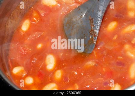 Gros plan sur les haricots cuits à la tomate maison cuisson dans la poêle à la vapeur et à la cuillère Banque D'Images