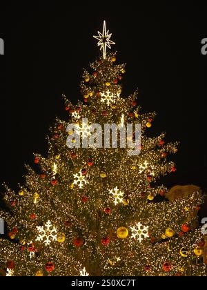 Sapin de Noël brillamment éclairé avec des ornements dorés, des boules rouges et des flocons de neige illuminés sur la place de Prague. Banque D'Images