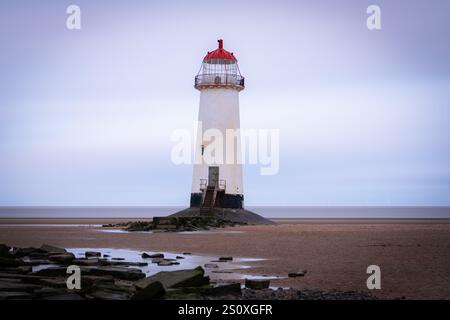 Phare blanc avec haut rouge debout sur la plage de sable avec des rochers et des flaques d'eau pendant la journée nuageuse Banque D'Images