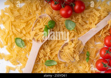 Pâtes Mafaldine crues non cuites avec des ingrédients pour la cuisson. Pâtes courtes italiennes Mafaldine à l'huile d'olive, tomates cerises, basilic, épices sur kitch blanc Banque D'Images