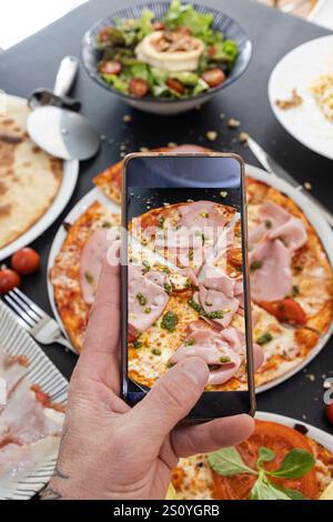 Main masculine faisant une photo de pizza avec un téléphone portable Banque D'Images