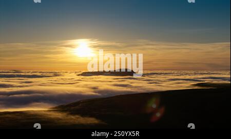 Ingleborough Hill apparaissant au-dessus d'une inversion de nuages un soir d'hiver contre le soleil couchant. North Yorkshire, Royaume-Uni. Banque D'Images