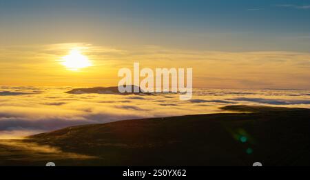 Ingleborough Hill apparaissant au-dessus d'une inversion de nuages un soir d'hiver contre le soleil couchant. North Yorkshire, Royaume-Uni. Banque D'Images