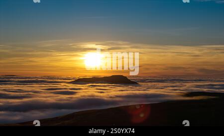 Ingleborough Hill apparaissant au-dessus d'une inversion de nuages un soir d'hiver contre le soleil couchant. North Yorkshire, Royaume-Uni. Banque D'Images