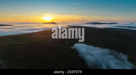 Ingleborough Hill apparaissant au-dessus d'une inversion de nuages un soir d'hiver contre le soleil couchant. North Yorkshire, Royaume-Uni. Banque D'Images