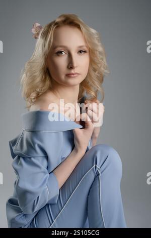 Jeune femme en vêtements bleus doux pose gracieusement sur un fond neutre Banque D'Images