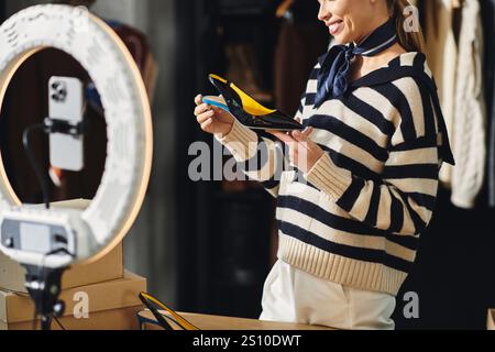 Jeune femme présente des chaussures et des tenues élégantes tout en filmant du contenu pour ses adeptes. Banque D'Images