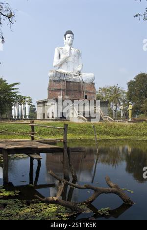 Une très grande statue de Bouddha se dresse près d'un étang à Wat Ek Phnom, un temple atmosphérique, partiellement ruiné du XIe siècle, à 11 km au nord de Battambang, au Cambodge. Banque D'Images