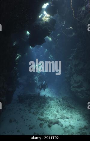 Un plongeur solitaire dans une grotte sous-marine sombre avec des rayons de lumière, site de plongée Dangerous Reef, St Johns Reef, Saint Johns, mer Rouge, Egypte, Afrique Banque D'Images