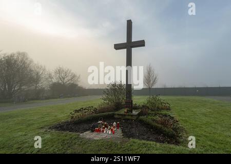 Simple croix en bois dans le cimetière brumeux avec des bougies votives rouges et blanches à sa base Banque D'Images