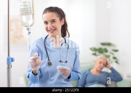 La jeune infirmière souriante ou le médecin aide la patiente âgée malade âgée à recevoir l'infusion goutte à goutte IV et la thérapie d'injection de vitamine assis sur le canapé en moi Banque D'Images