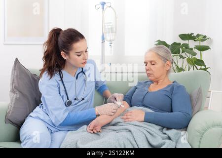 La jeune infirmière amicale ou le médecin aide la femme âgée malade patient dans la réception de perfusion goutte à goutte IV et la thérapie d'injection de vitamine assis sur le canapé dans M. Banque D'Images