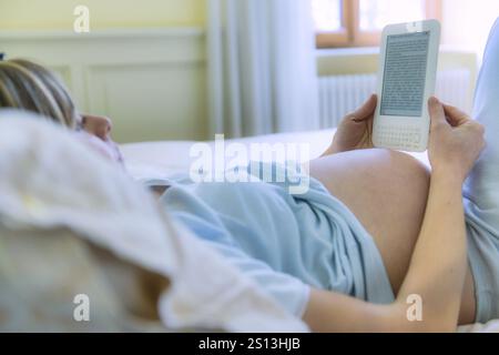 Une femme caucasienne enceinte lit au lit Banque D'Images